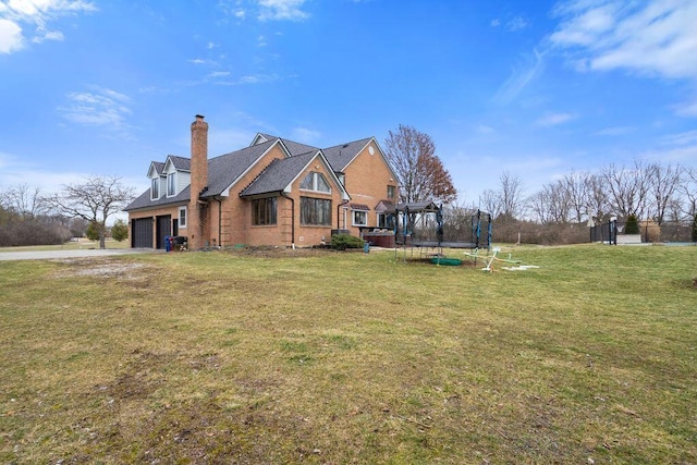 exterior space with a chimney, an attached garage, a trampoline, a yard, and brick siding