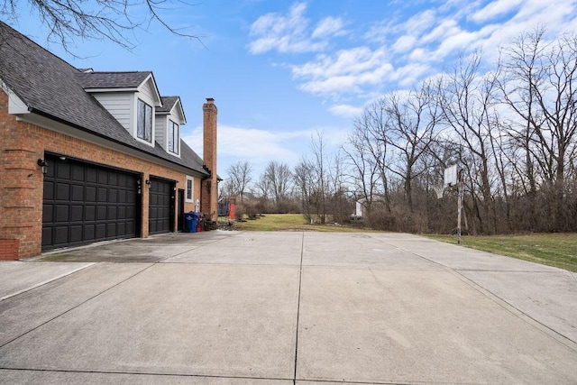 exterior space with roof with shingles, brick siding, a chimney, and concrete driveway