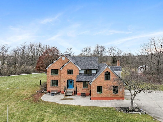 traditional-style house with brick siding, roof with shingles, a chimney, a front yard, and a patio area