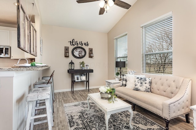 living room with lofted ceiling, light wood-type flooring, a ceiling fan, and baseboards