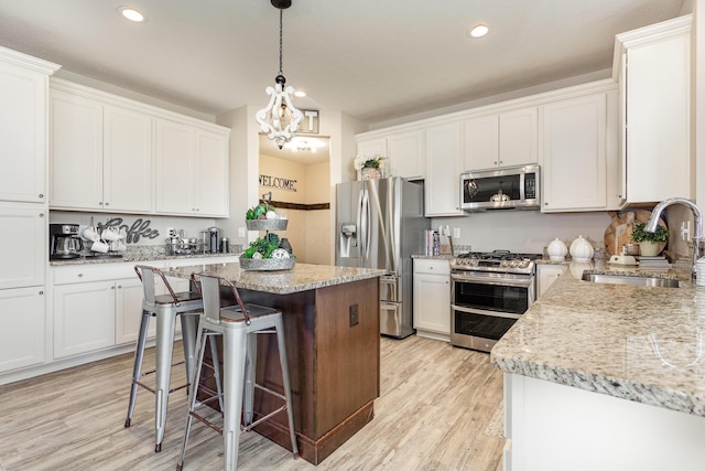 kitchen with light stone counters, stainless steel appliances, a sink, white cabinetry, and a center island