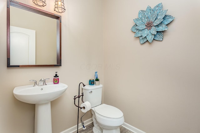 half bathroom featuring a sink, toilet, baseboards, and wood finished floors