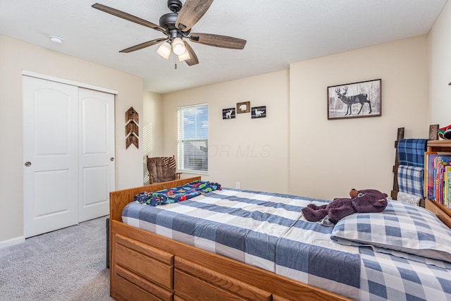 bedroom with a textured ceiling, a ceiling fan, a closet, and light colored carpet