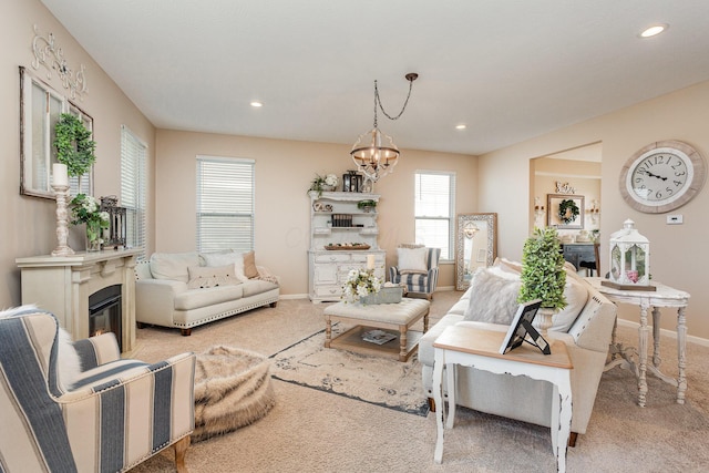 living room featuring light carpet, baseboards, a notable chandelier, and a glass covered fireplace