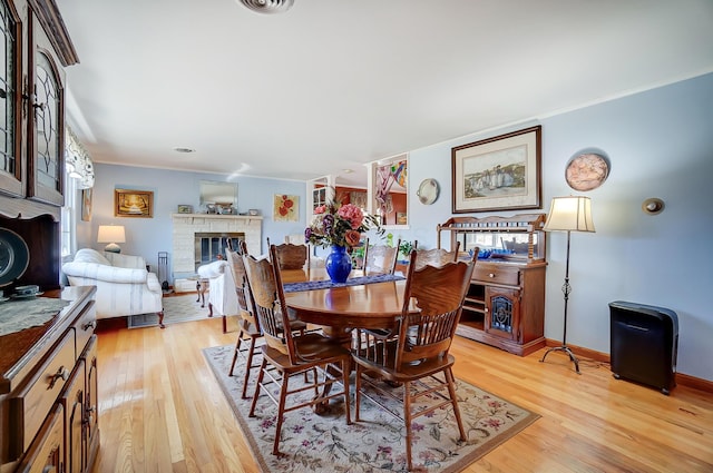 dining room featuring ornamental molding, a glass covered fireplace, and light wood-type flooring