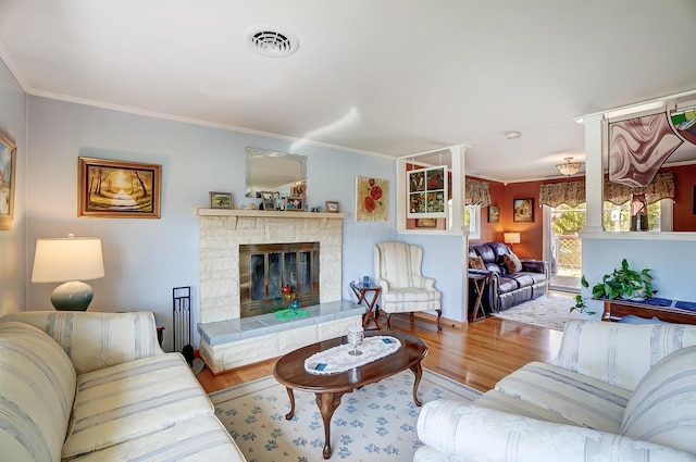 living area featuring visible vents, crown molding, a stone fireplace, and wood finished floors