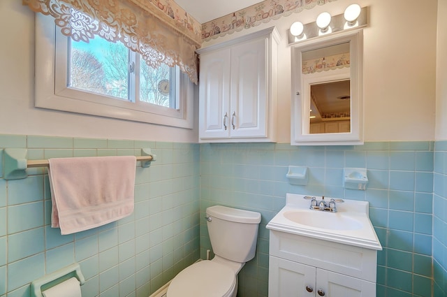 half bath featuring toilet, wainscoting, vanity, and tile walls