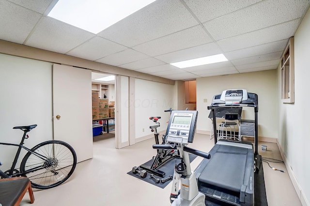 workout room featuring a paneled ceiling and baseboards