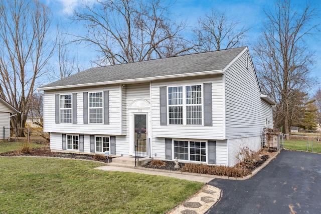 split foyer home with a front yard, roof with shingles, and fence