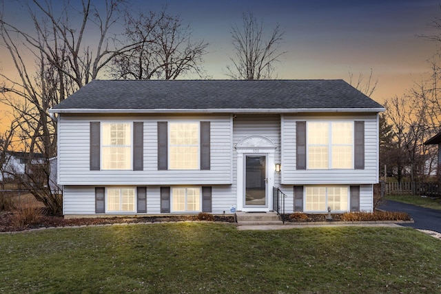 bi-level home featuring entry steps, a yard, and a shingled roof