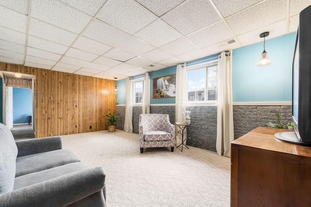 sitting room with carpet floors, visible vents, wood walls, and a drop ceiling