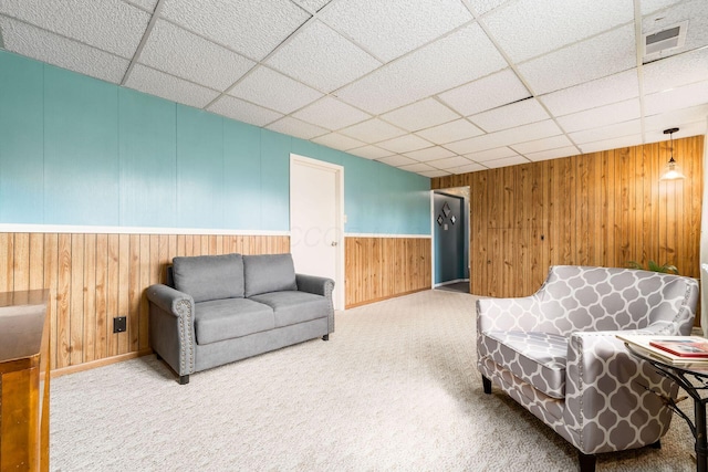 sitting room featuring carpet, visible vents, a drop ceiling, and wooden walls