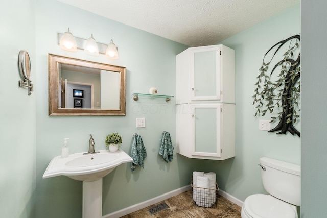 bathroom with toilet, a textured ceiling, visible vents, and baseboards