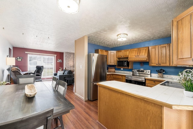 kitchen featuring tile counters, appliances with stainless steel finishes, open floor plan, wood finished floors, and a sink