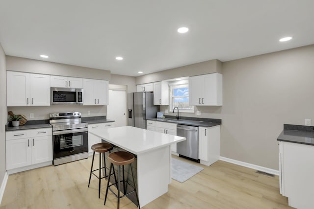 kitchen featuring appliances with stainless steel finishes, a breakfast bar area, dark countertops, and white cabinets