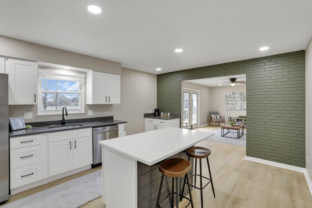 kitchen with brick wall, appliances with stainless steel finishes, open floor plan, white cabinetry, and a sink