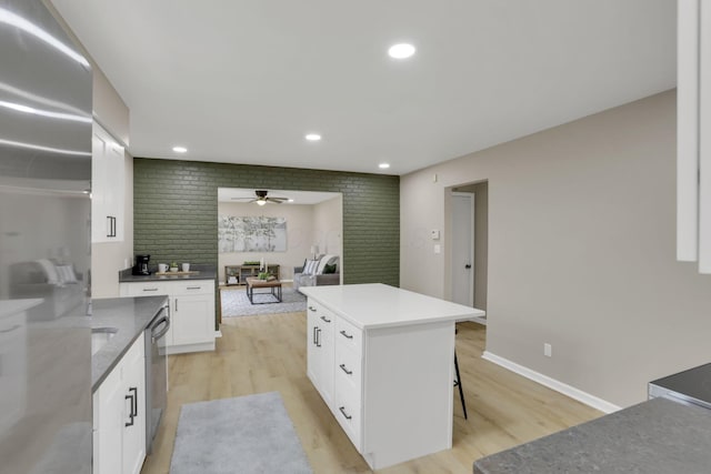 kitchen with light wood finished floors, stainless steel appliances, white cabinets, a kitchen island, and a kitchen breakfast bar