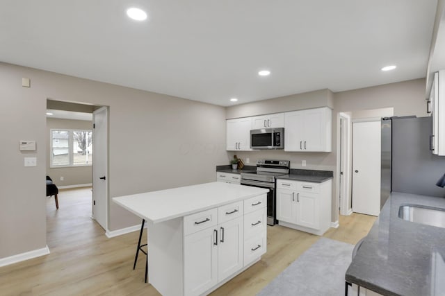 kitchen featuring light wood finished floors, a kitchen island, white cabinetry, and stainless steel appliances