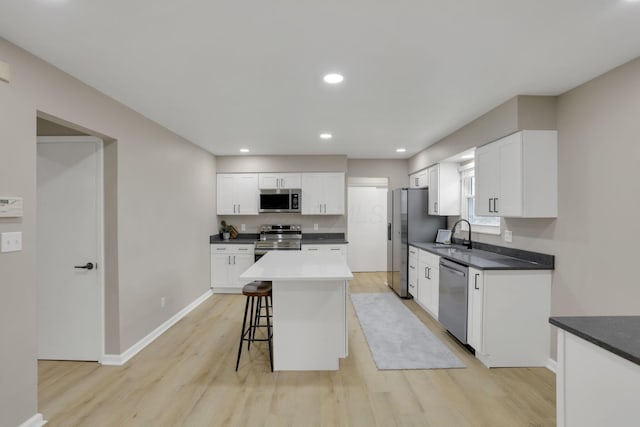 kitchen featuring stainless steel appliances, a kitchen island, light wood-style floors, white cabinets, and a kitchen bar