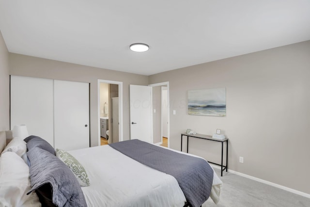 bedroom with baseboards, a closet, ensuite bathroom, and light colored carpet