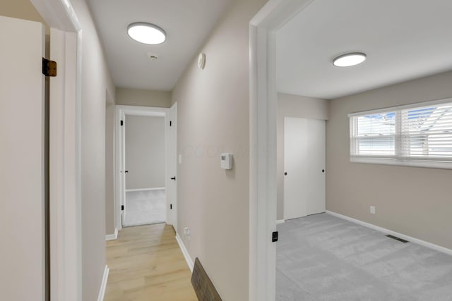 corridor featuring visible vents, baseboards, and light colored carpet