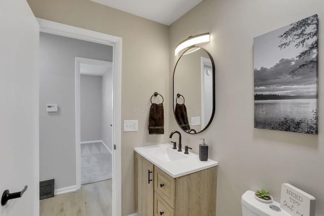 half bath featuring visible vents, toilet, vanity, wood finished floors, and baseboards