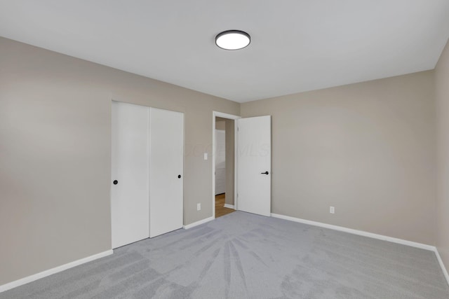 unfurnished bedroom with a closet, light colored carpet, and baseboards