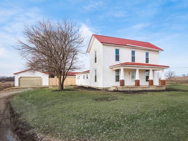 view of front facade with covered porch, metal roof, a front lawn, and an outbuilding