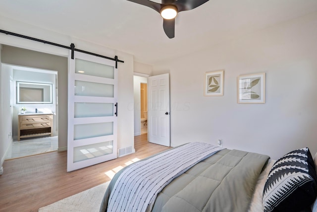 bedroom with a barn door, wood finished floors, a ceiling fan, visible vents, and baseboards