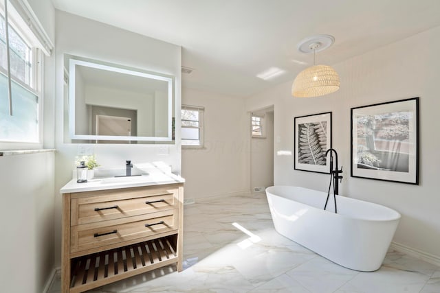 bathroom featuring marble finish floor, a freestanding tub, vanity, and baseboards