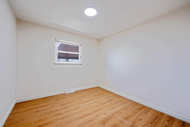 spare room with wood finished floors, visible vents, and baseboards