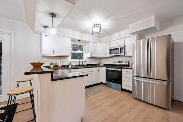 kitchen with stainless steel appliances, a peninsula, a sink, light wood-style floors, and pendant lighting