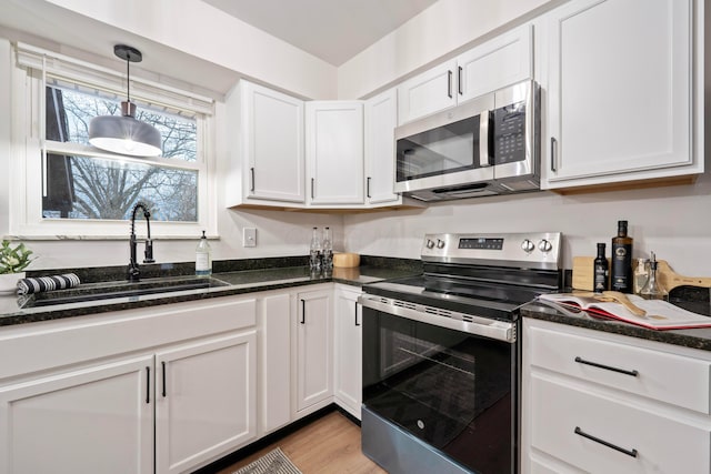 kitchen featuring white cabinets, appliances with stainless steel finishes, decorative light fixtures, light wood-type flooring, and a sink