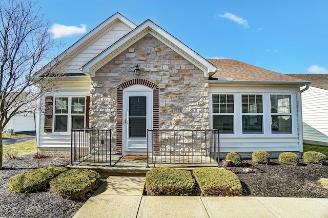 view of front of home with stone siding, roof with shingles, and covered porch