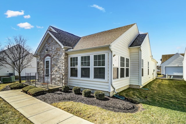 view of front facade with stone siding, roof with shingles, and a front yard