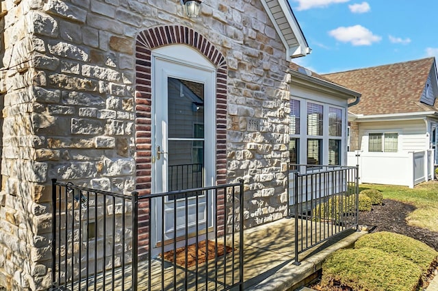 entrance to property featuring stone siding and a shingled roof