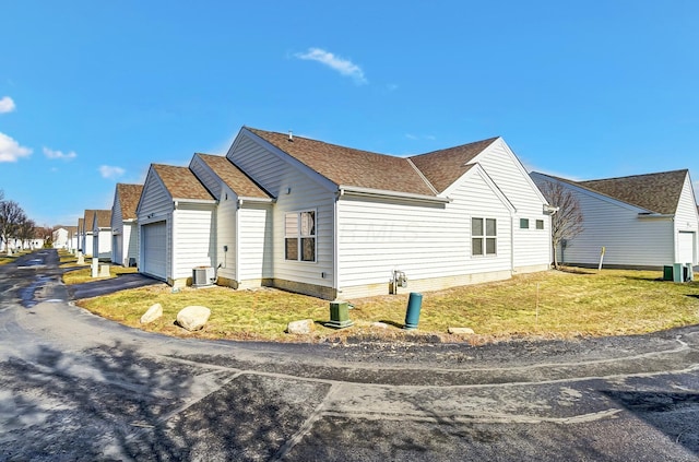 view of side of property with a garage, roof with shingles, a lawn, and central air condition unit