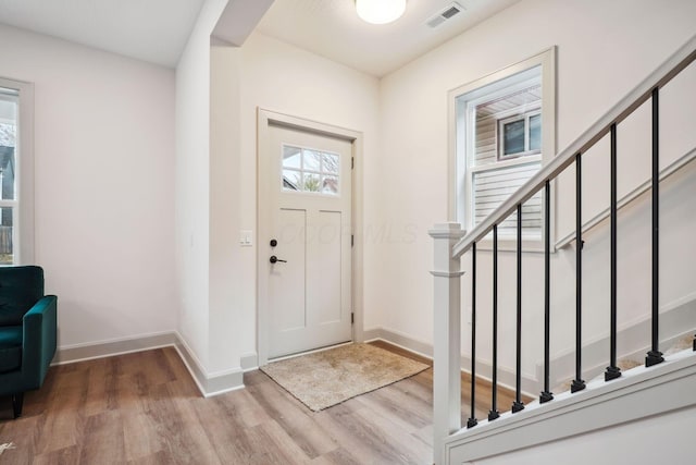 foyer entrance with baseboards, stairs, visible vents, and wood finished floors