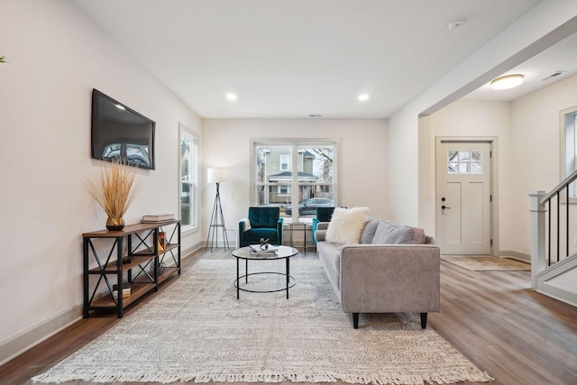 living area with stairway, wood finished floors, visible vents, and baseboards