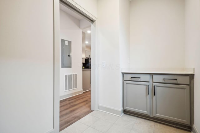 hallway with electric panel, visible vents, baseboards, and light tile patterned floors