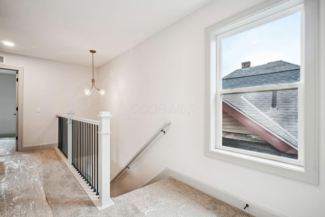 corridor with an inviting chandelier, carpet, baseboards, and an upstairs landing