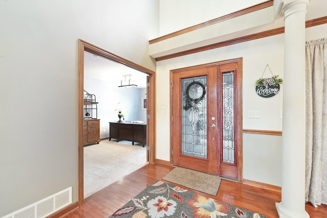 foyer entrance featuring visible vents, decorative columns, baseboards, and wood finished floors