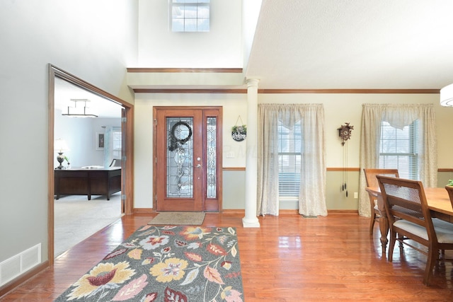 entryway featuring decorative columns, a high ceiling, visible vents, and wood finished floors