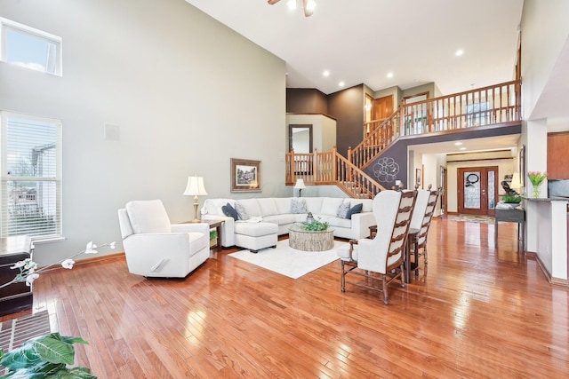 living room featuring a towering ceiling, light wood-type flooring, plenty of natural light, and stairway