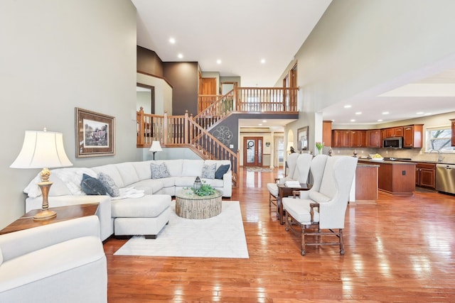 living area featuring stairway, recessed lighting, a towering ceiling, and light wood-style floors