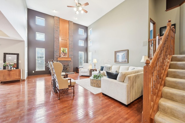 living area with a fireplace, wood-type flooring, stairway, a towering ceiling, and ceiling fan