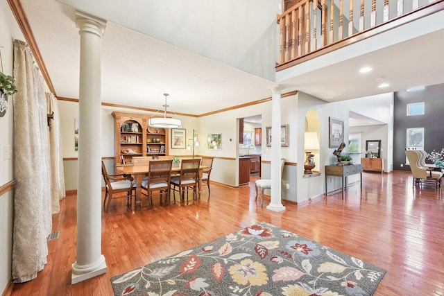 dining area with wood finished floors, a towering ceiling, baseboards, decorative columns, and crown molding