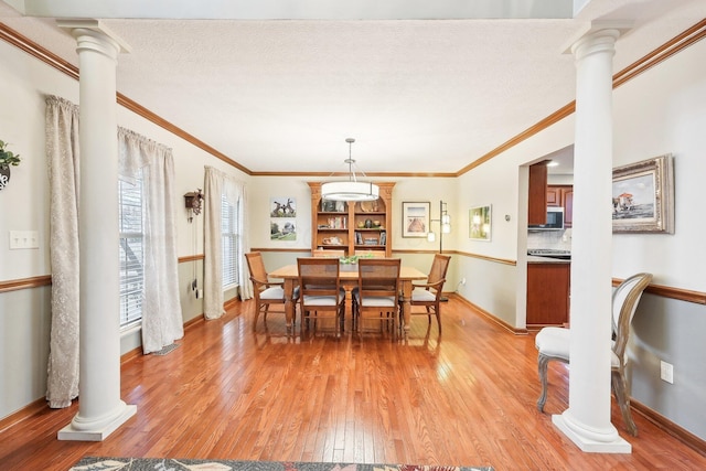 dining space featuring light wood finished floors, baseboards, ornamental molding, a textured ceiling, and ornate columns