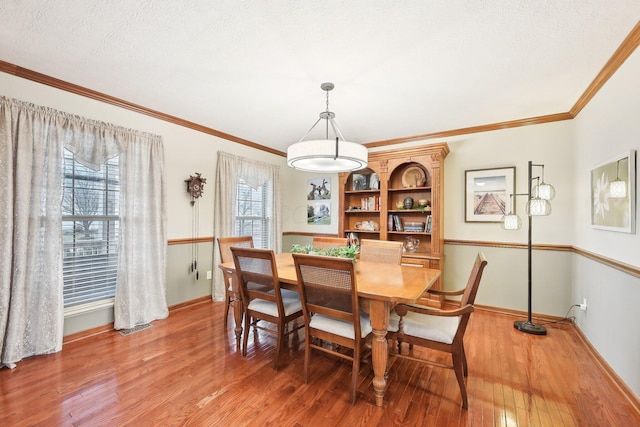 dining area with a textured ceiling, ornamental molding, light wood-style flooring, and baseboards