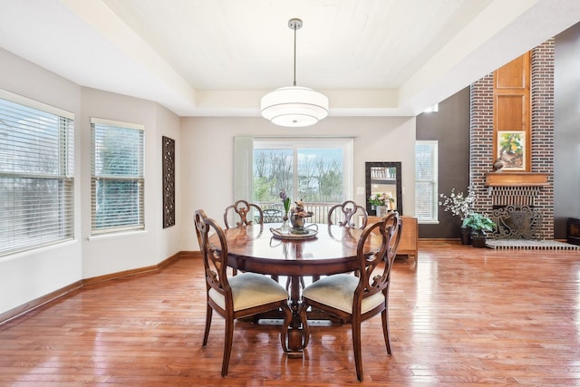 dining area featuring light wood-style floors, a tray ceiling, and baseboards